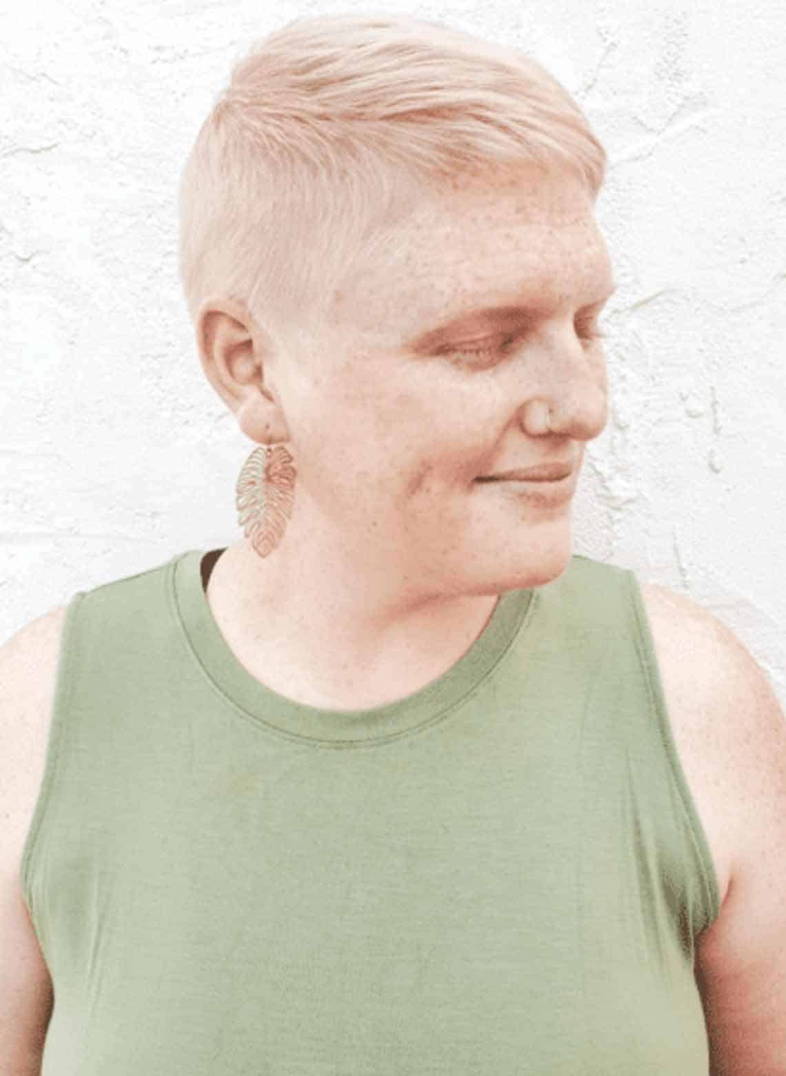 person wearing green tank top looking to the side with eyes closed, hair is blonde with a pixie cut