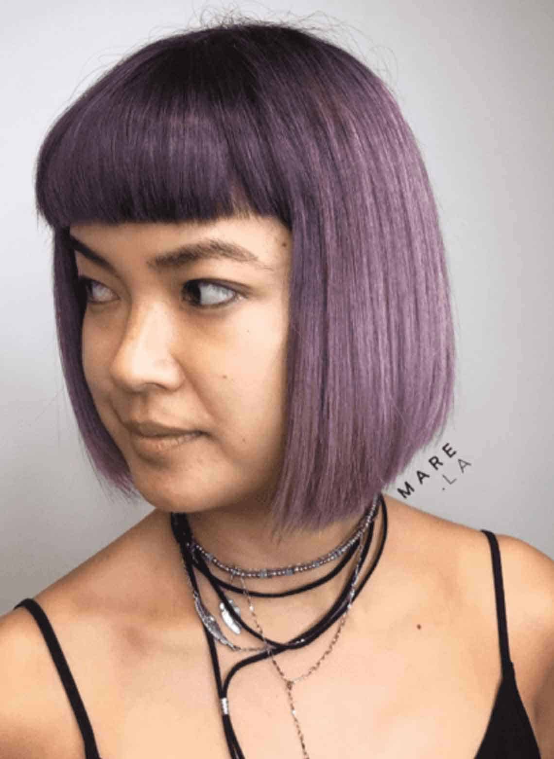 person wearing black tank top, lots of necklaces, with purple hair cut in a blunt bob 