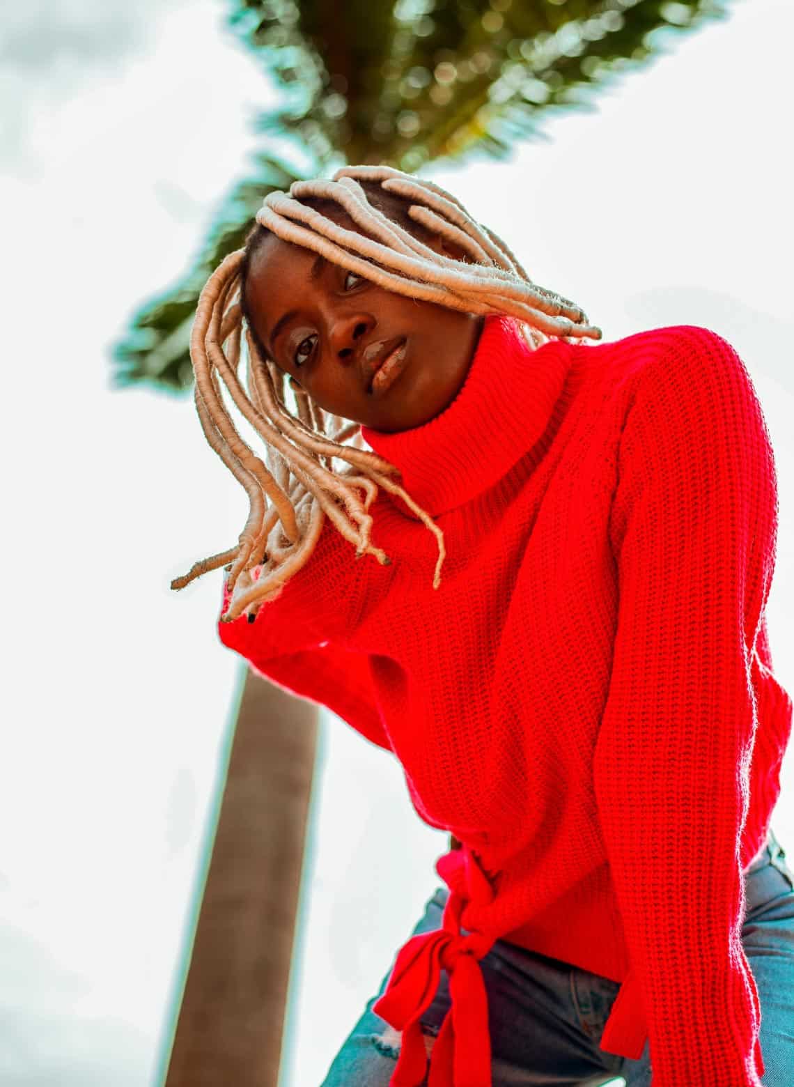 person wearing bright red turtle neck sweater and jeans with long blonde faux locs