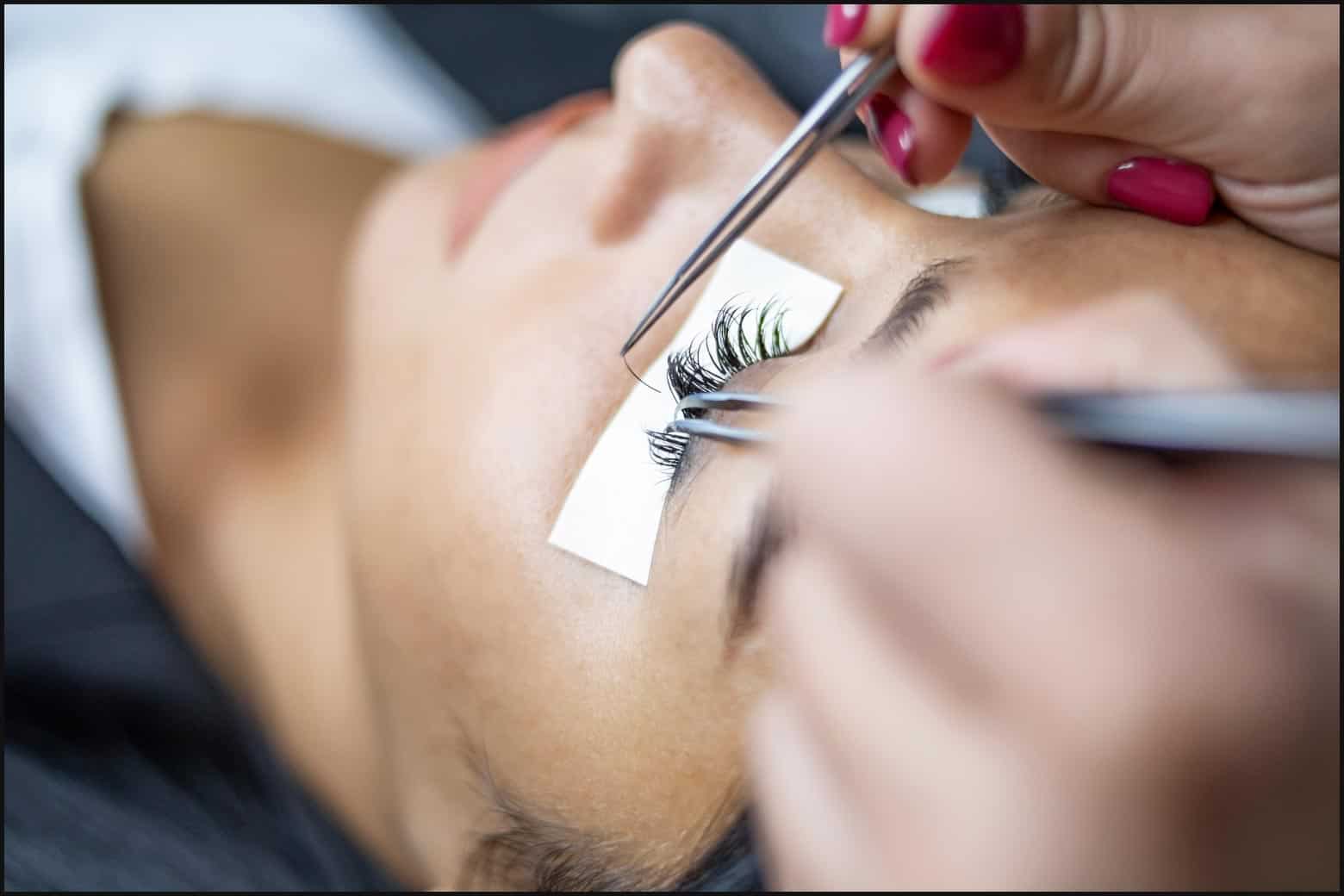 person laying down with under-eye patches while lash tech applies lash extensions
