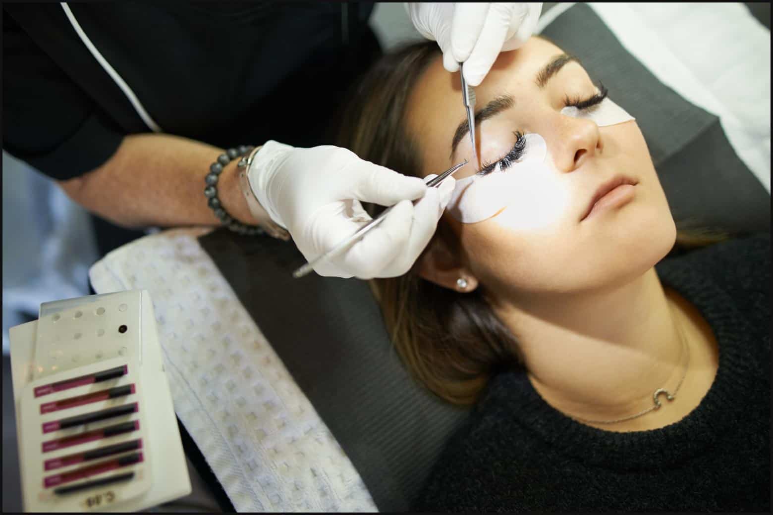person laying down with under-eye patches while lash tech applies lash extensions