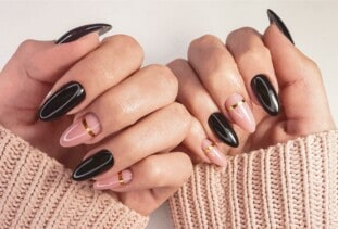 close up of black and pink nails with subtle gold design, brown sleeves showing along wrists