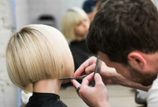 person with short blonde bob getting a haircut at the salon