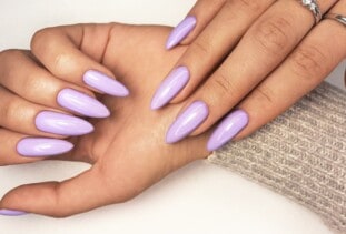 close up of long purple acrylic nails with the arm covered by a light brown sweater sleeve