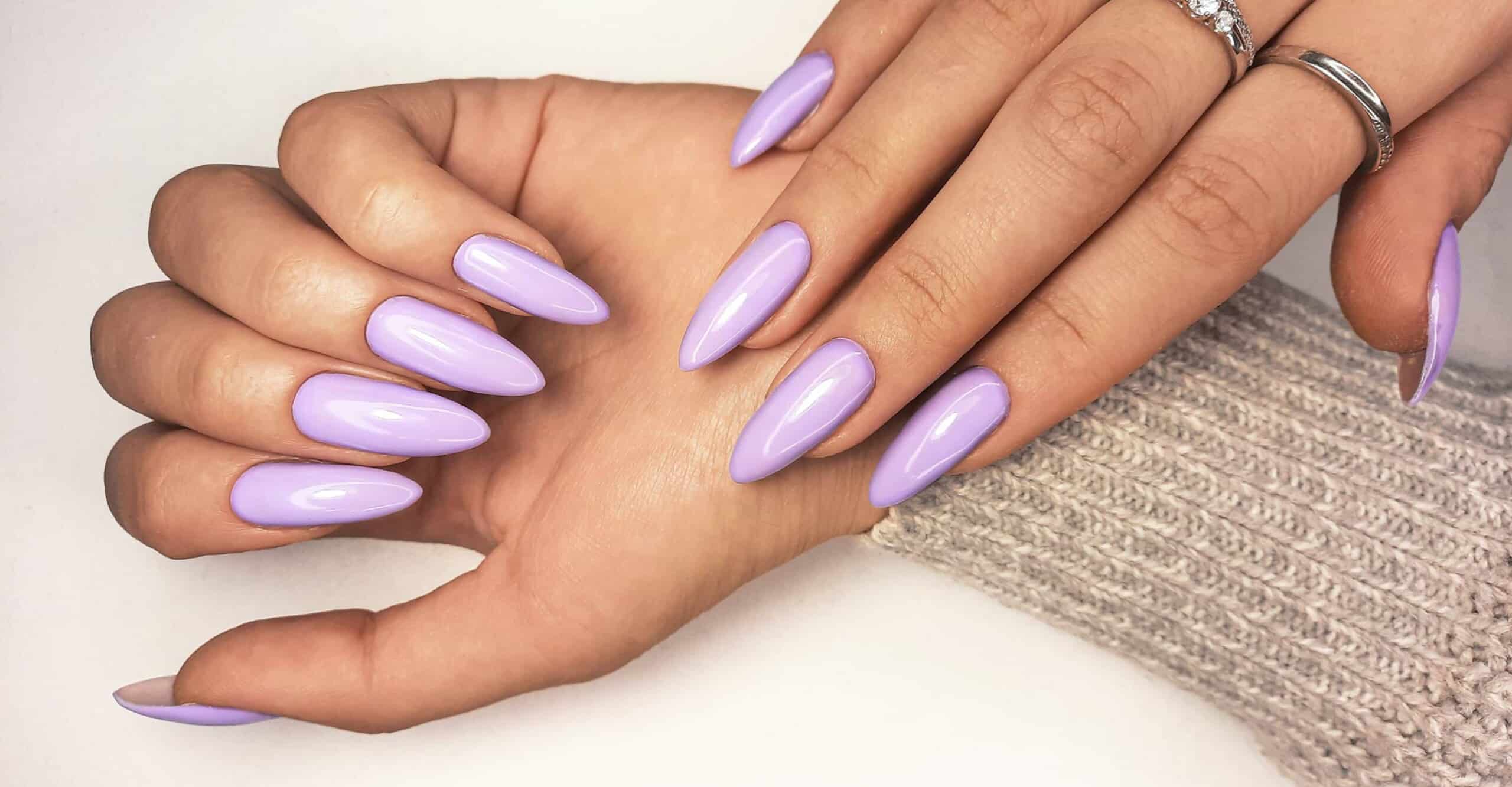 close up of long purple acrylic nails with the arm covered by a light brown sweater sleeve
