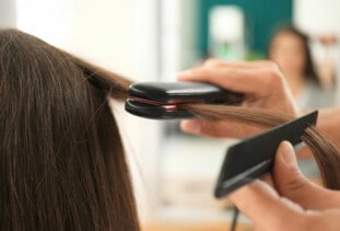 close up of stylist flat-ironing a client's brunette hair in a salon
