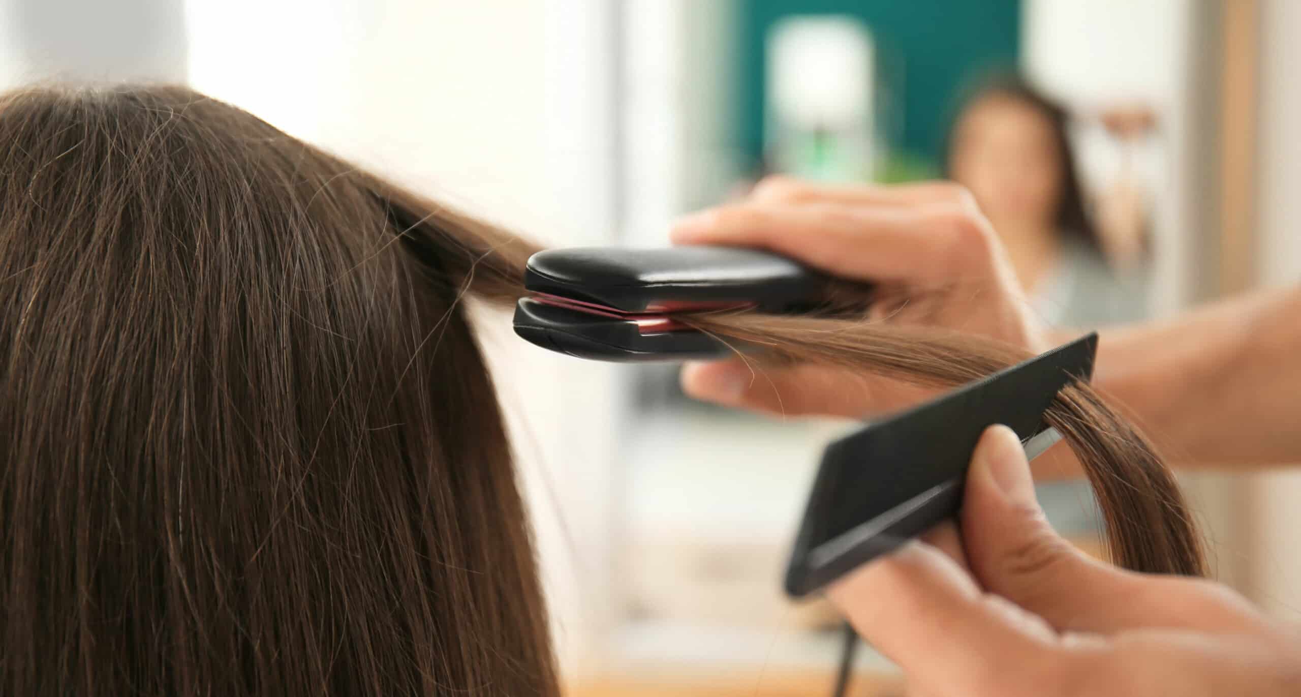 close up of stylist flat-ironing a client's brunette hair in a salon