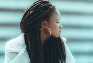 person with faux locs, big hoop earrings, nose piercing, and white furry jacket looking to the side