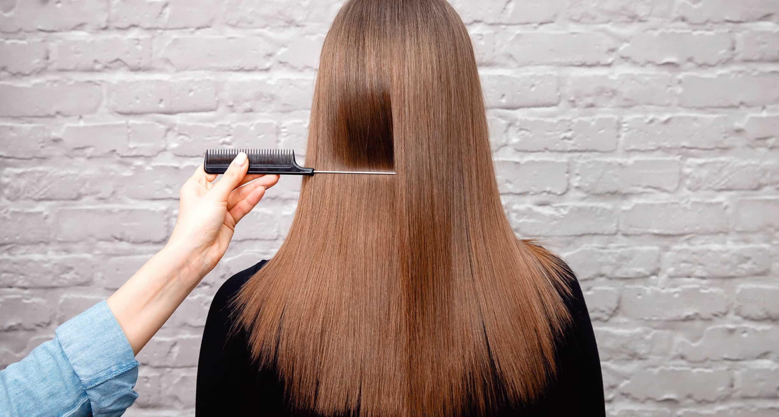 back of person's straight and long brunette hair, hand holding a comb against the hair