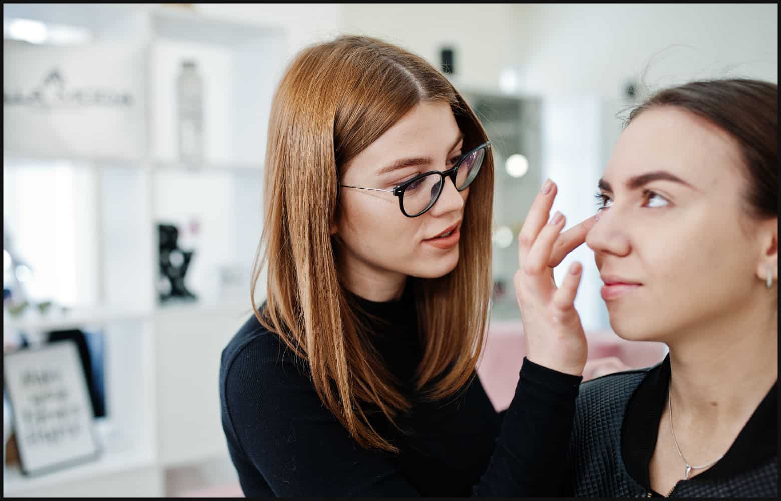 Brunette makeup artists wearing glasses applying makeup to client’s cheeks in the salon