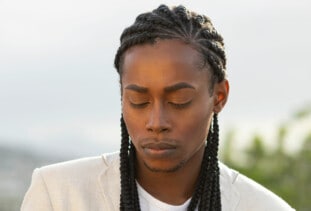 person with long cornrows wearing a white shirt and looking down