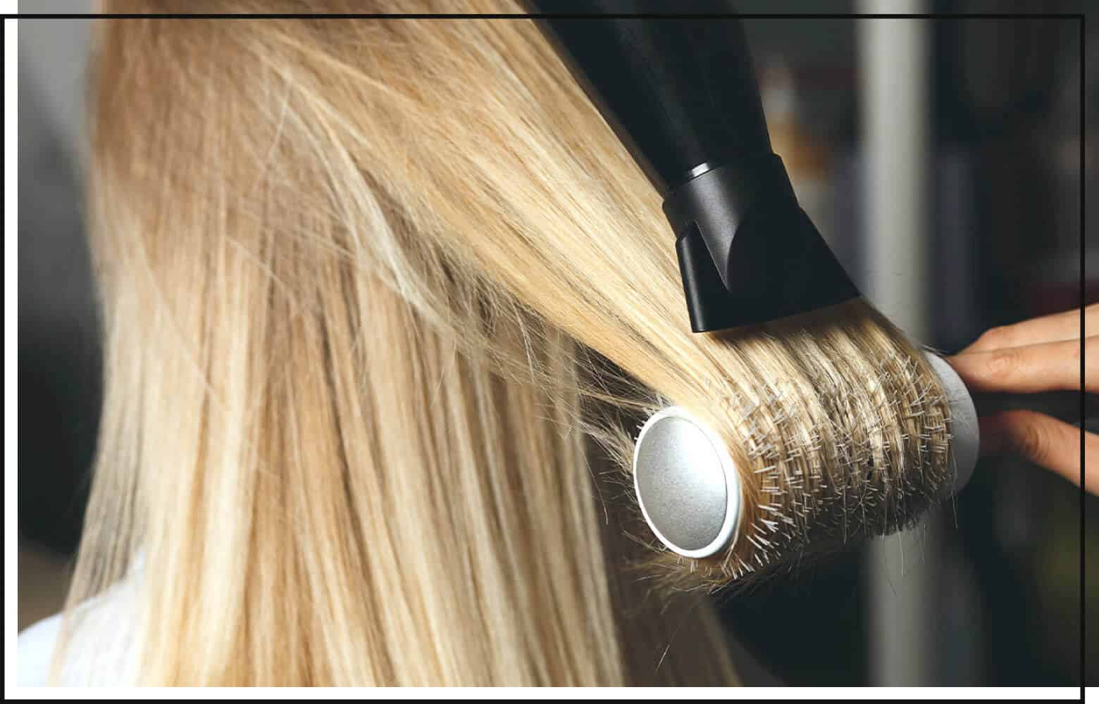 close up of stylist blow drying blonde hair with a round brush