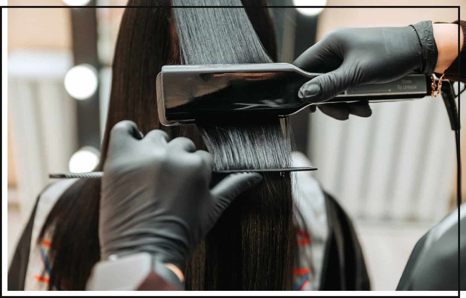 stylist flat ironing and combing client's black hair in the salon
