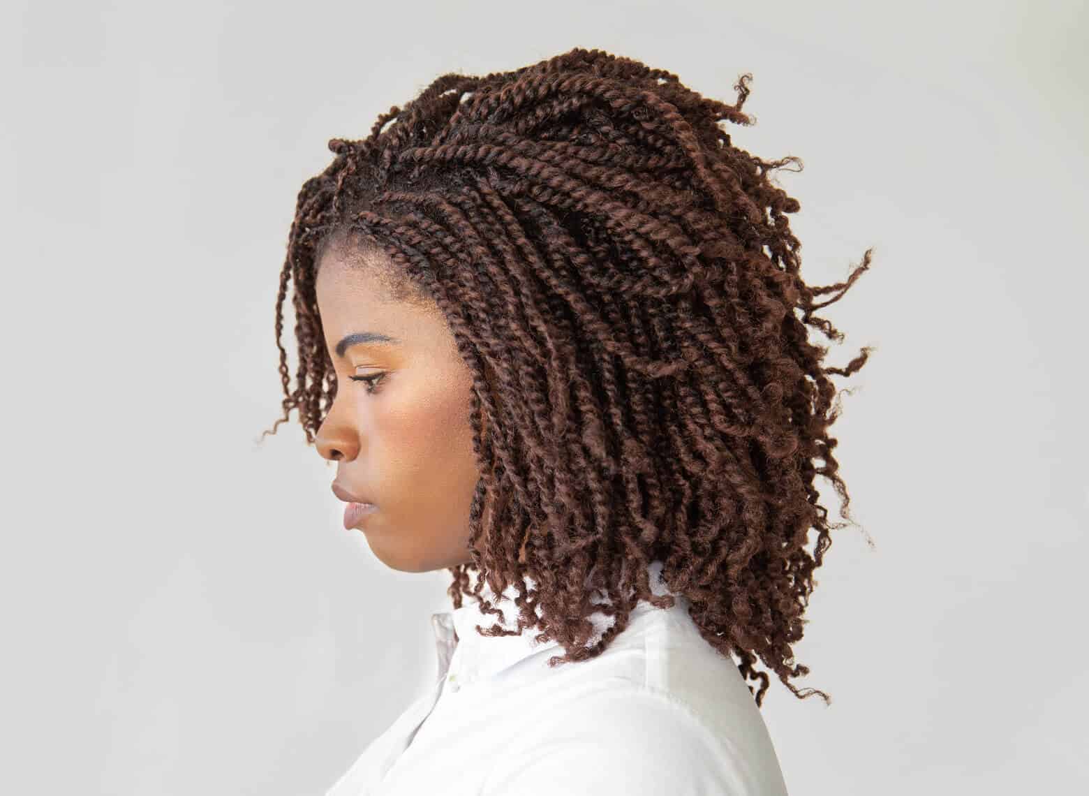 profile of person with brown shoulder-length nubian twists, looking down, and wearing a white button-up top