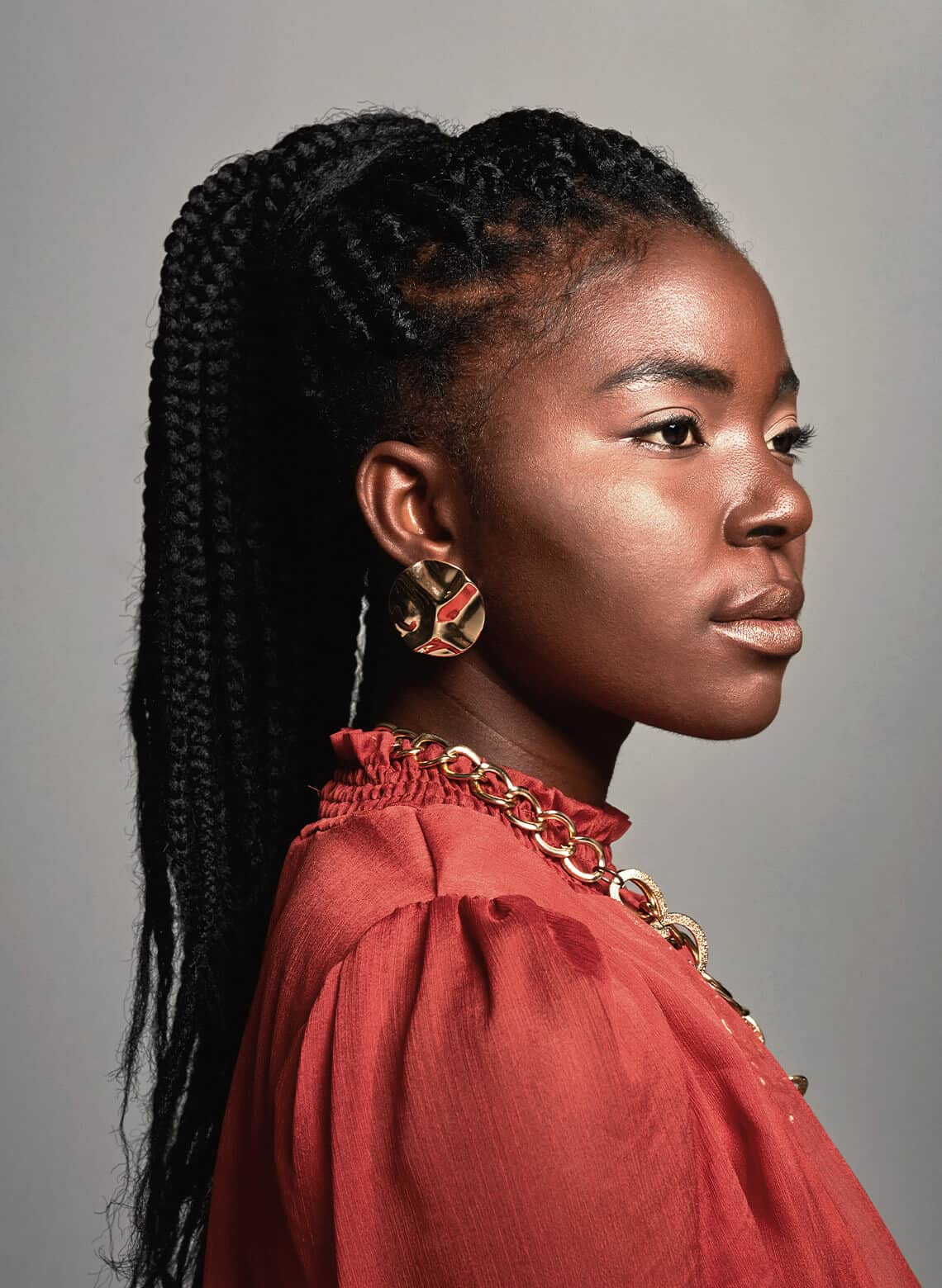 person looking to the right with a long braided ponytail, chunky jewelry, and a red blouse