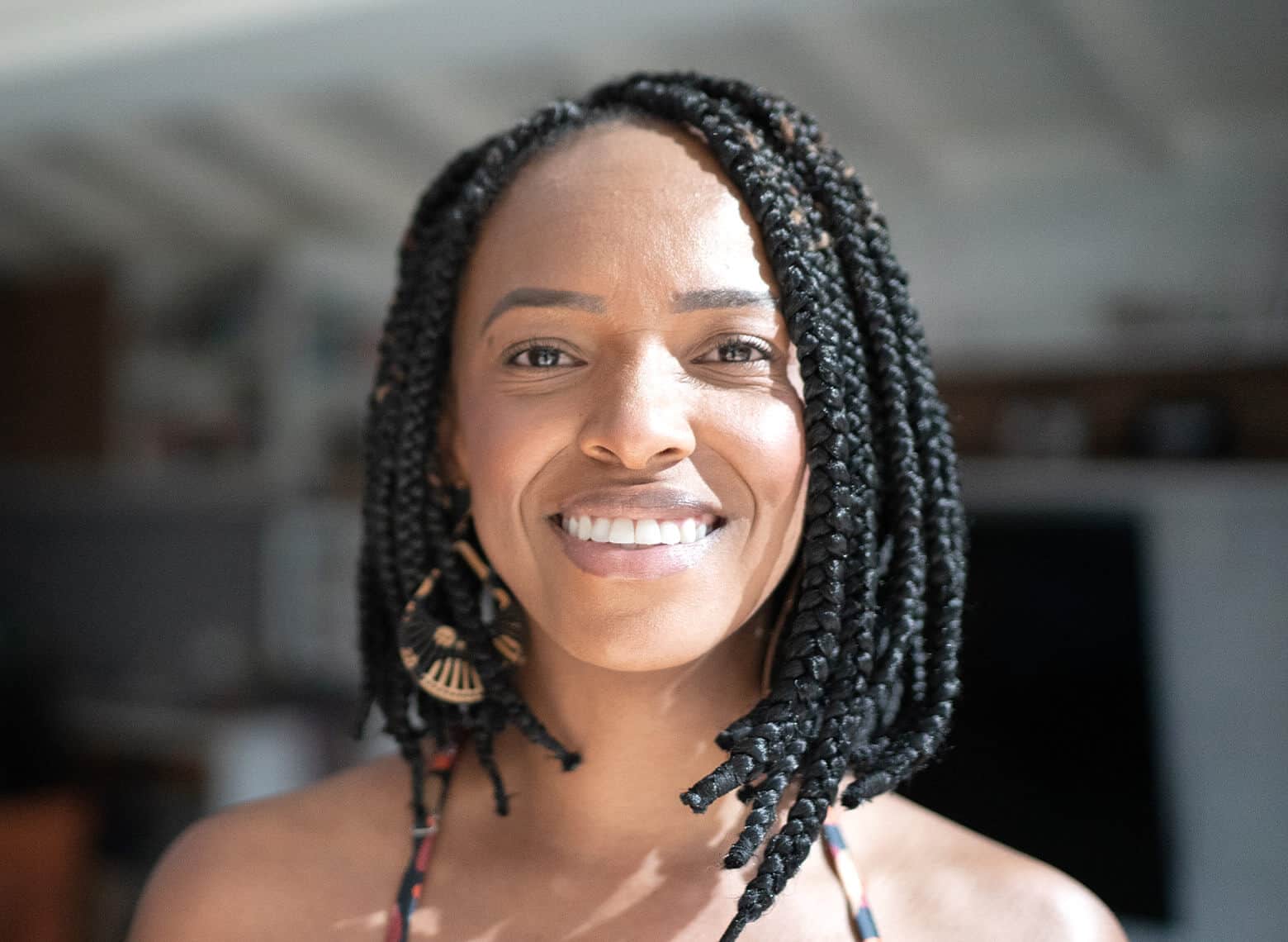 smiling person with braided bob and wearing teardrop-shaped earrings