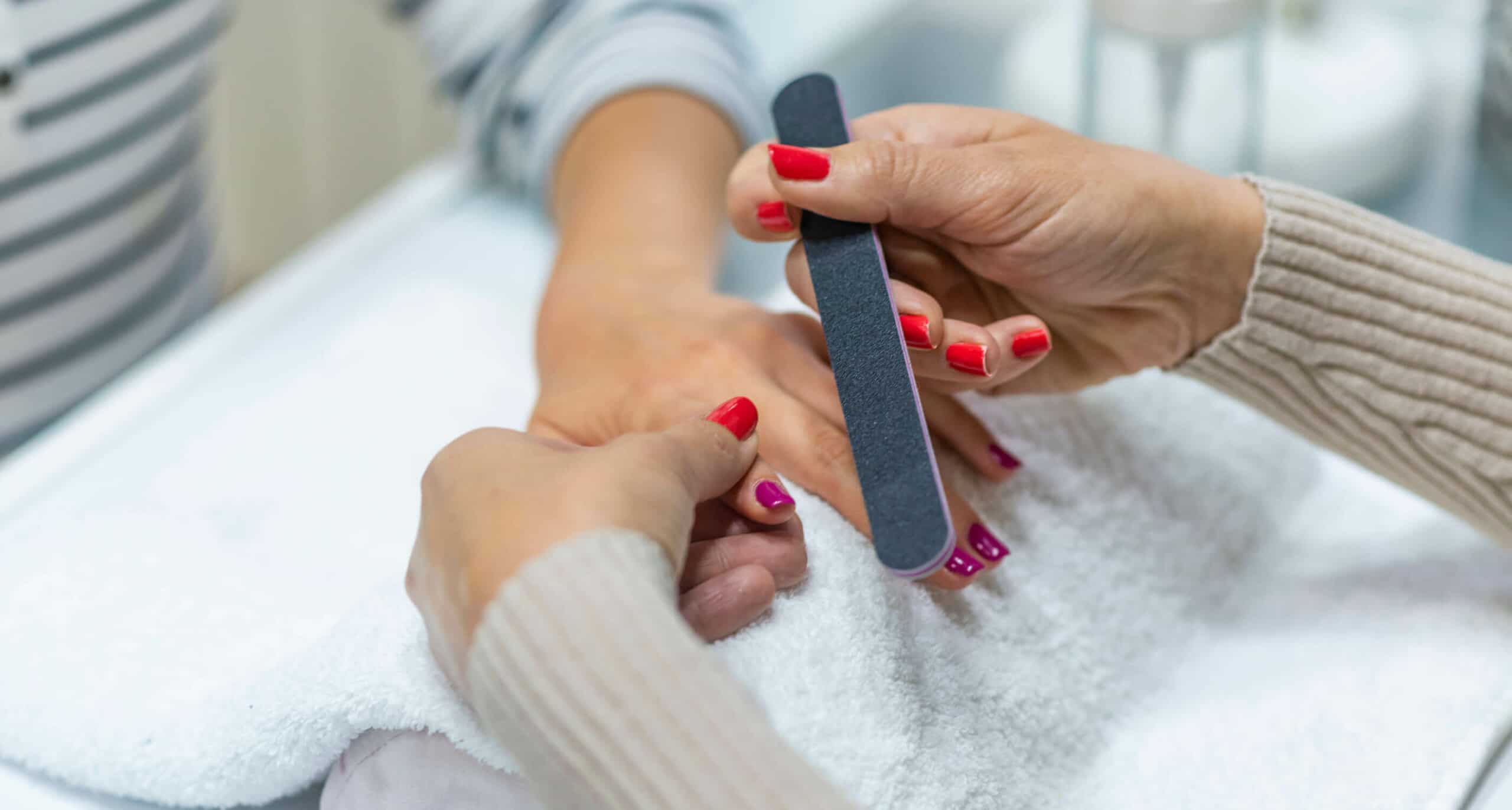 close up of manicurist holding client’s hands and nail file over white towel
