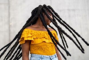 person wearing yellow off-the-shoulder-top and light blue jeans swinging long dreads