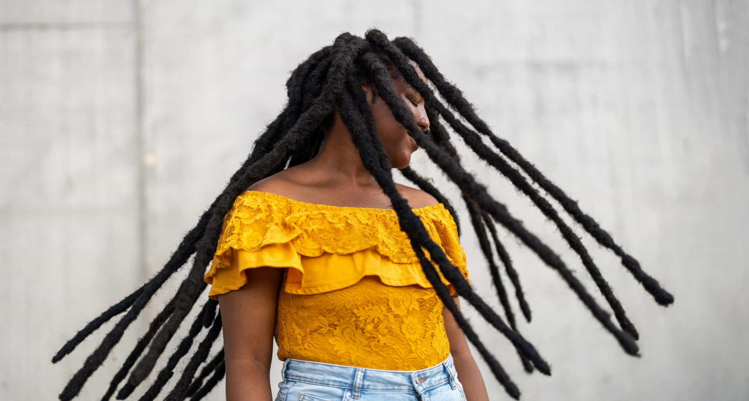 person wearing yellow off-the-shoulder-top and light blue jeans swinging long dreads