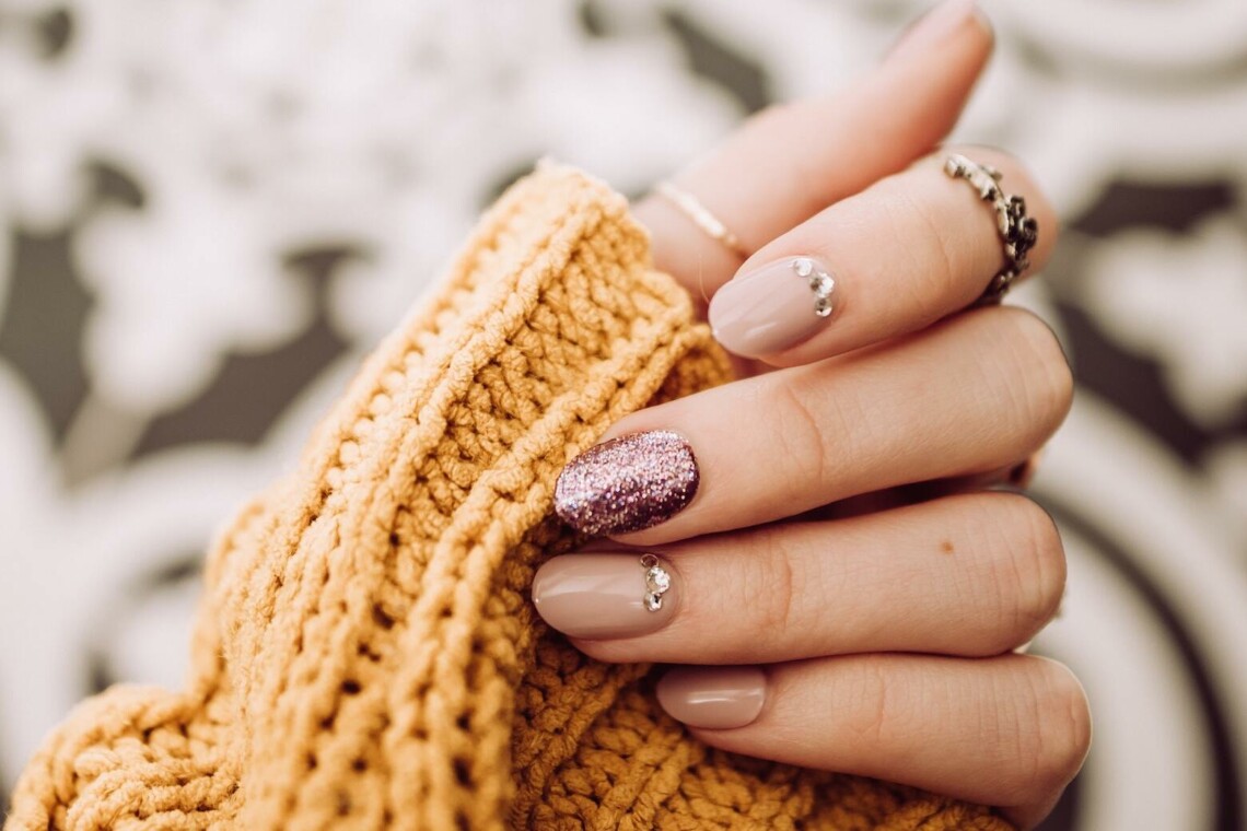 pink sparkly manicure holding yellow sweater