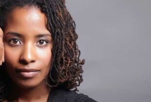 person with shoulder-length sisterlocks straight ahead with hand on face