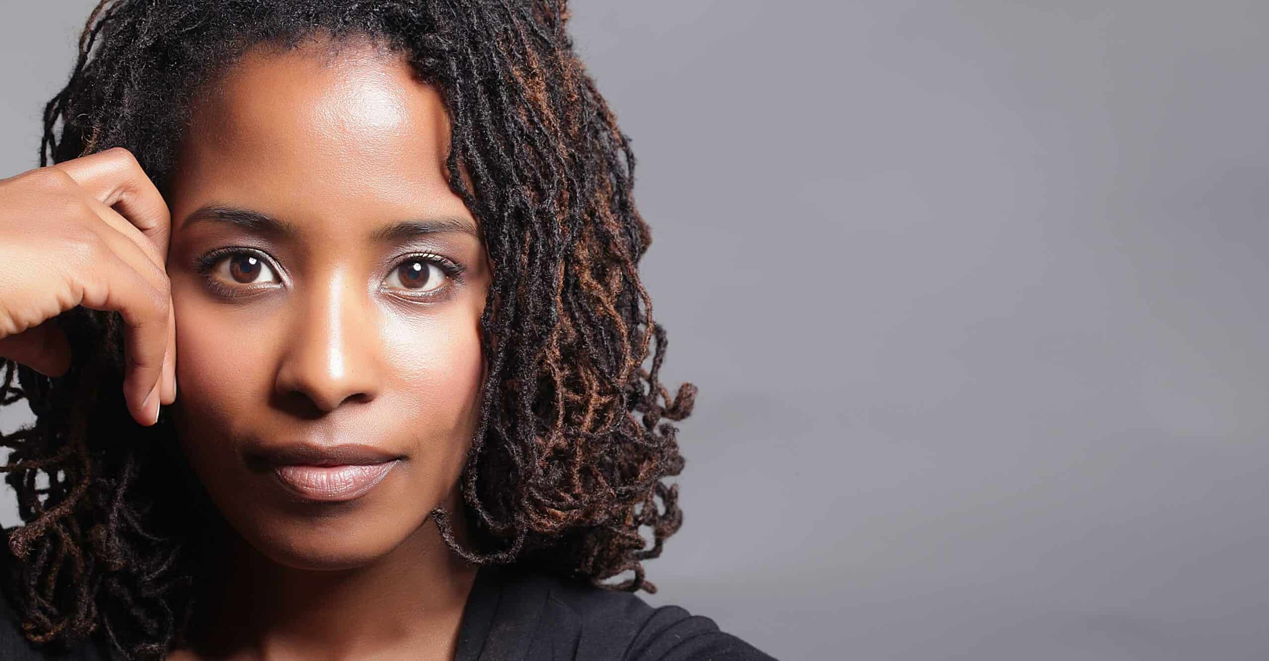 person with shoulder-length sisterlocks straight ahead with hand on face