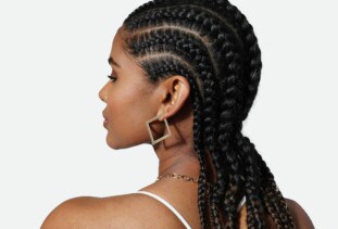 backside of a person’s head with long stitch braids wearing geometric earrings and a gold chain necklace