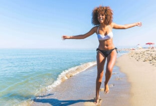 happy woman running along the beach wearing a white bikini top and black bikini bottoms