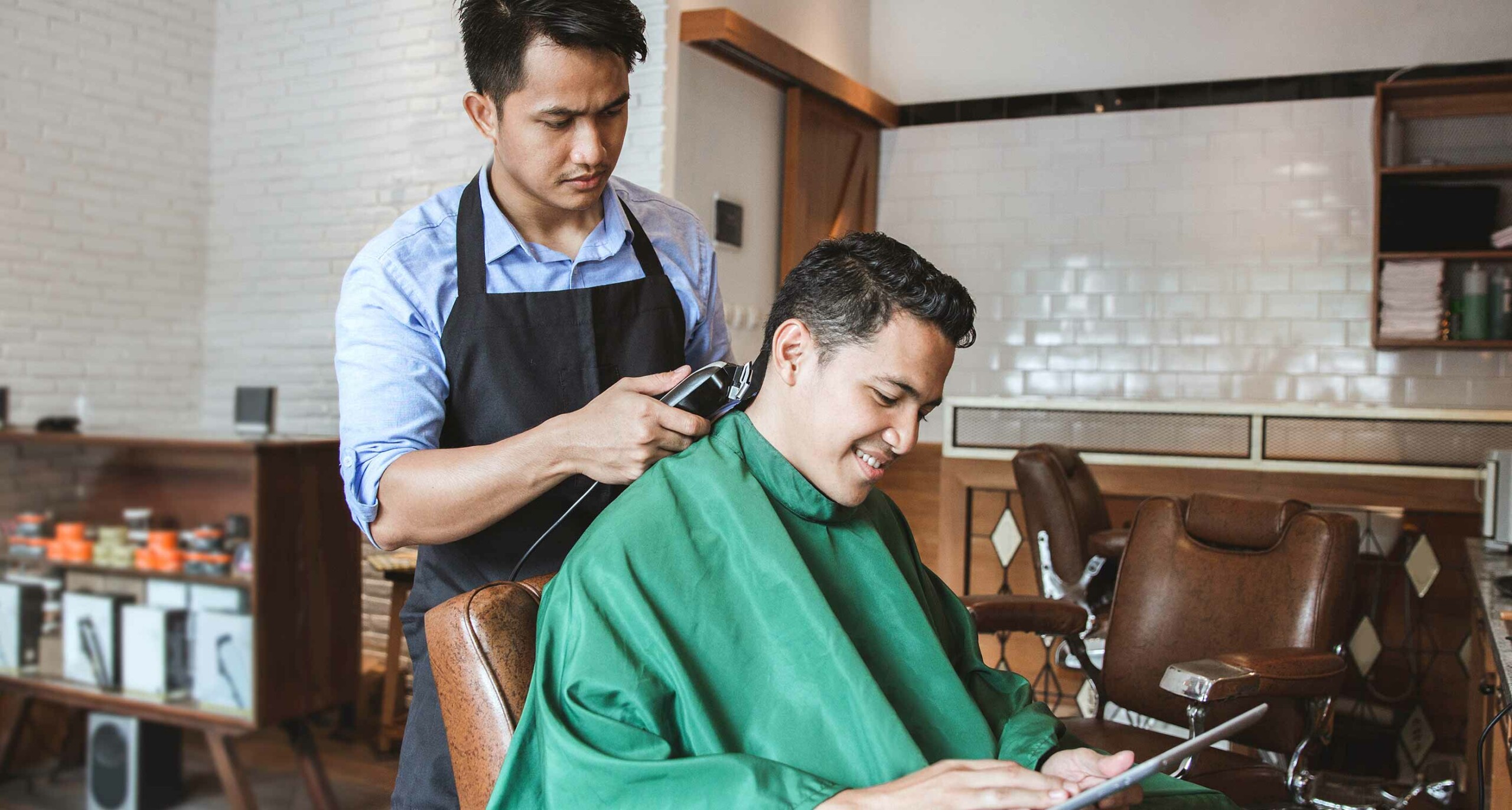 barber wearing blue button down and black smock shaving neck of client in a barbershop
