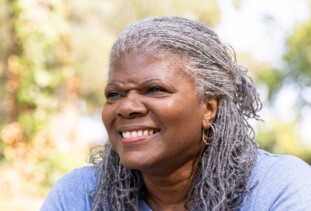 smiling person with grey sisterlocks, double hoop earrings, and a grey shirt
