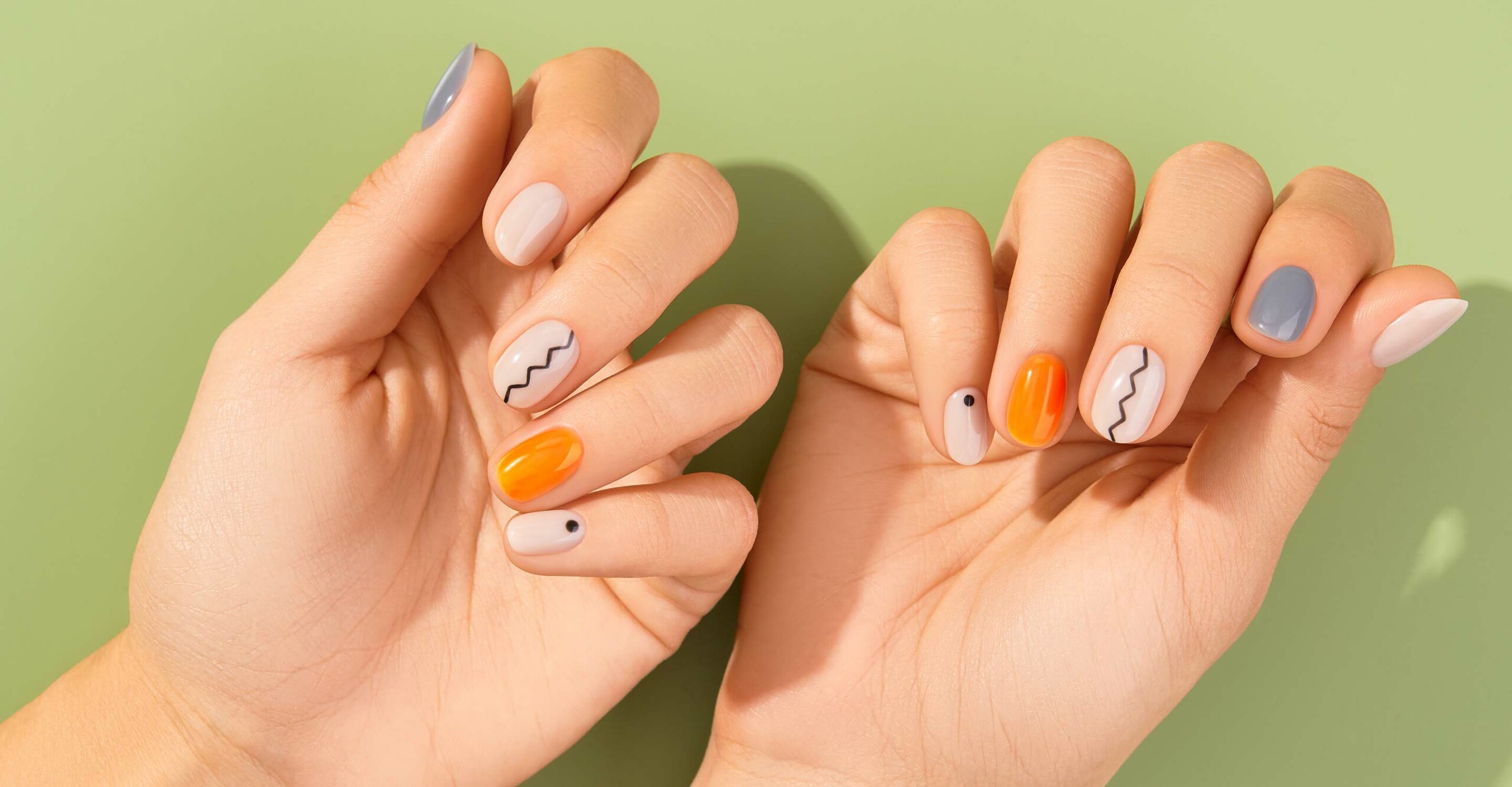 two hands with pearl, orange, grey and patterned nails against a light green background