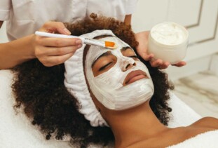close-up on person with naturally coily hair, laying down and getting a facial applied in a salon