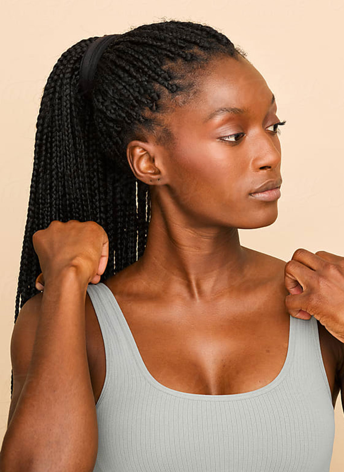 person wearing grey tank top with hair in long ponytail box braids, looking off to the side with hands adjusting tank to straps