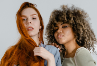 woman with straight red hair and woman with curly brown and blonde hair posing