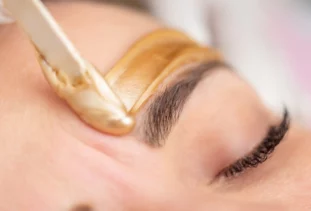 Esthetician applies wax to help shape client’s eyebrows.