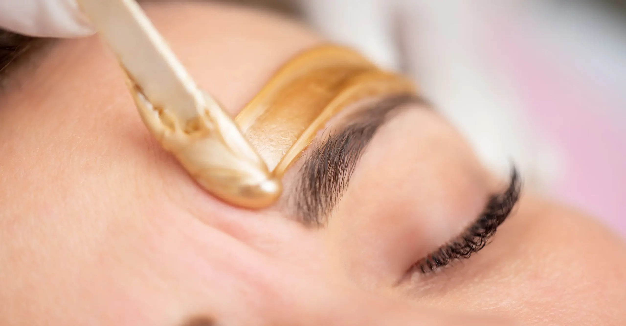 Esthetician applies wax to help shape client’s eyebrows.