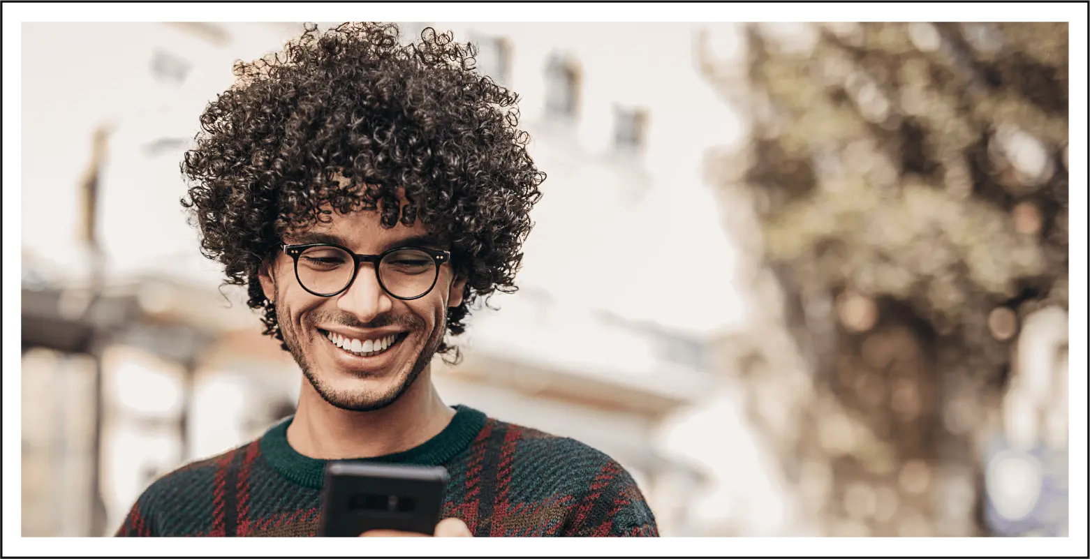 Man with defined curls smiling down at phone.