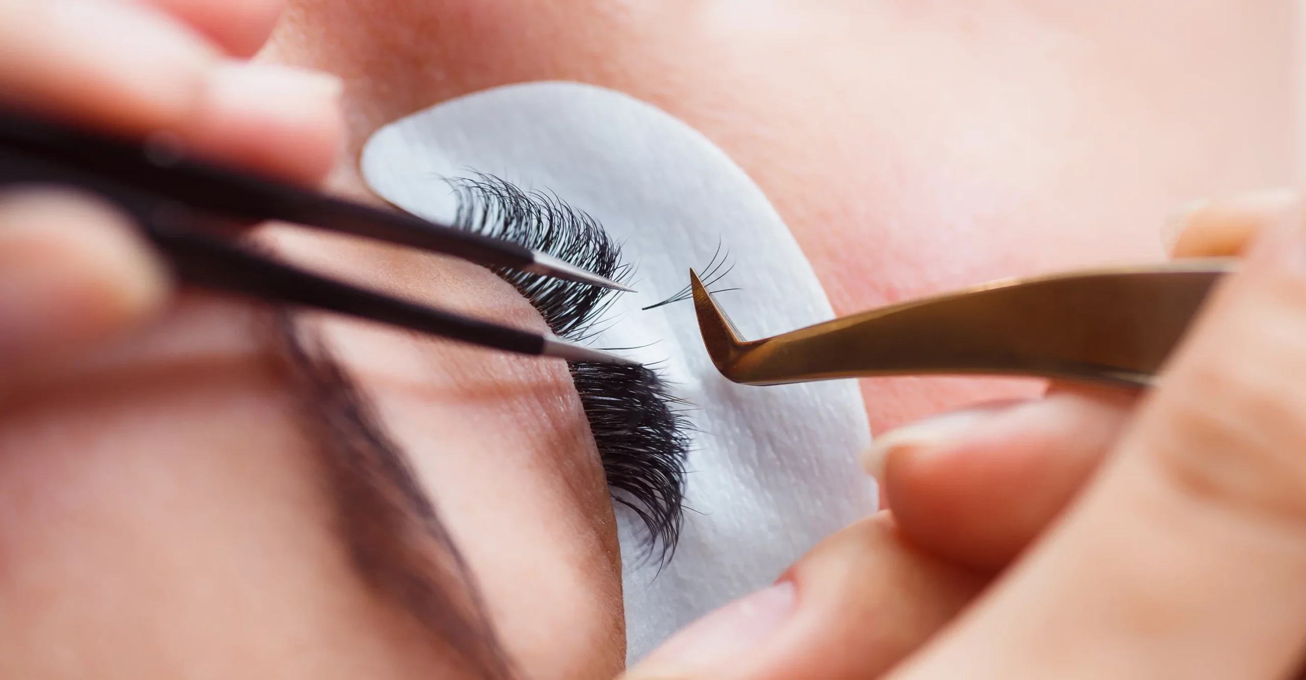 A lash technician uses tweezers to apply lash extensions to a client’s natural lashes.