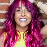 person with pink and purple ombre hair smiling with yellow shirt