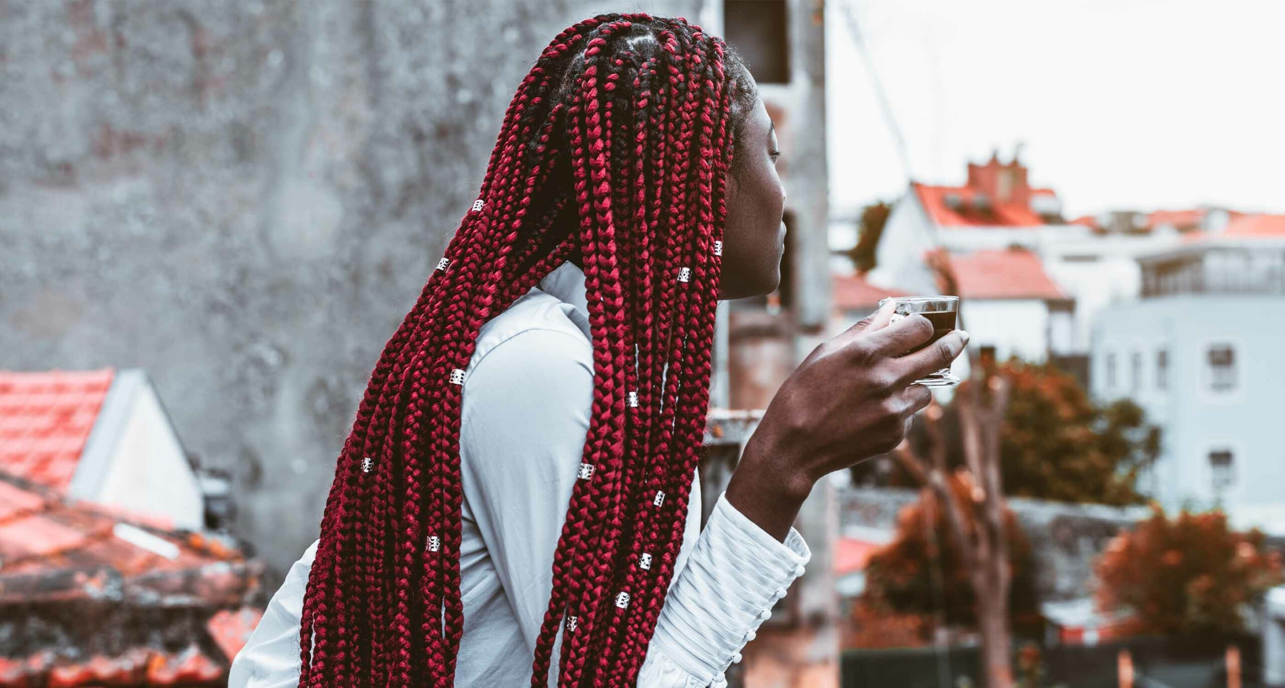 woman with red braids and hair jewelry looking away from camera holding a cup
